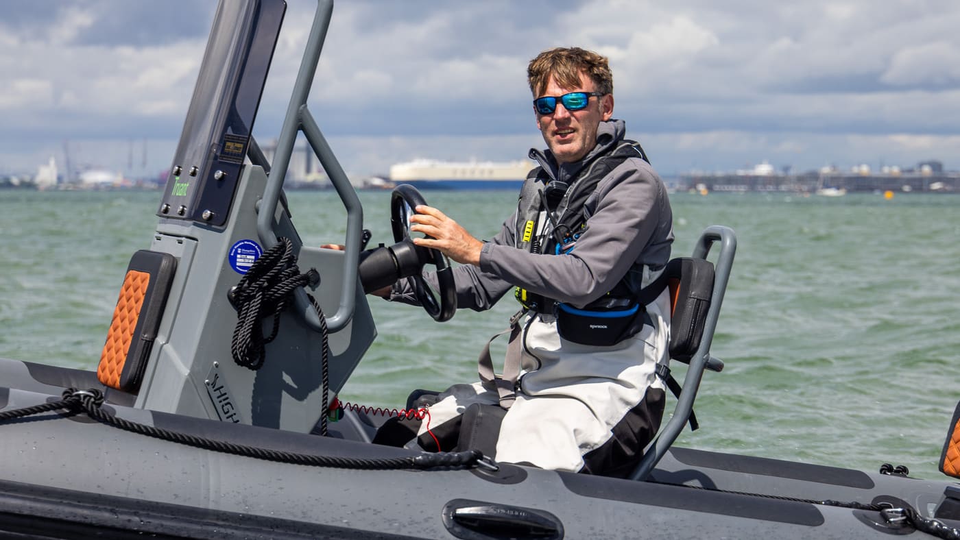 Skipper at the console of a grey RIB on the Solent with Southampton Water shipping behind