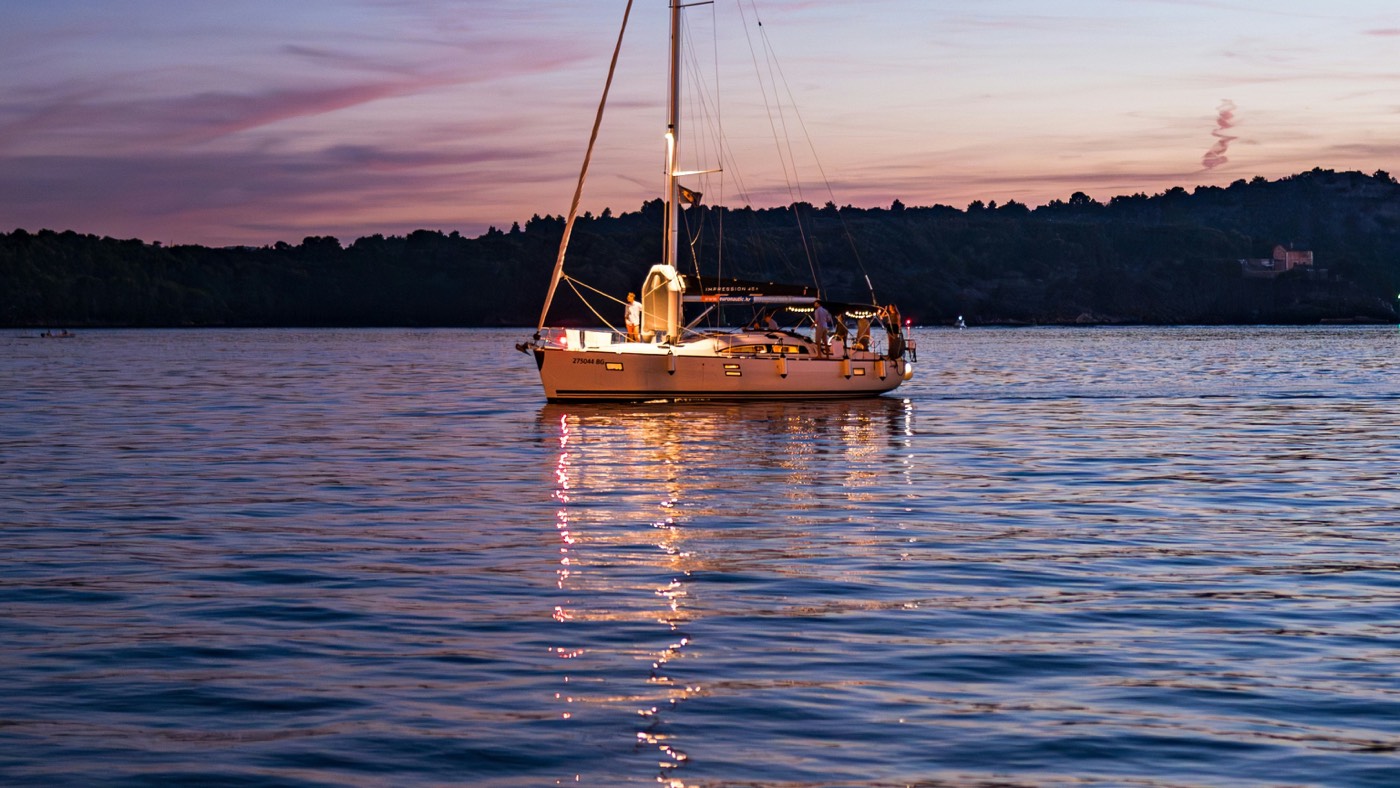 Cruising yacht under way at dusk with crew on deck and navigation lights on, ready for a night sail