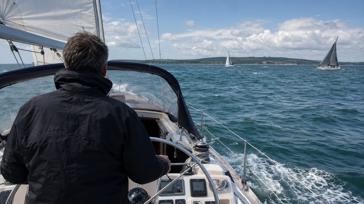 Helming a cruising yacht on the Solent with the Isle of Wight and other yachts ahead