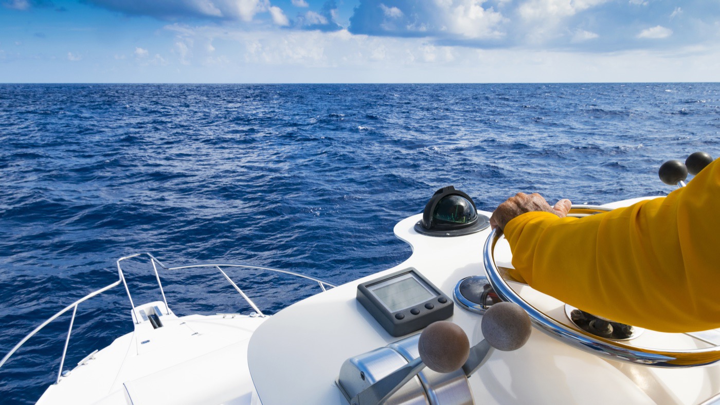 Hand on the wheel beside the engine throttles, steering under power in open water