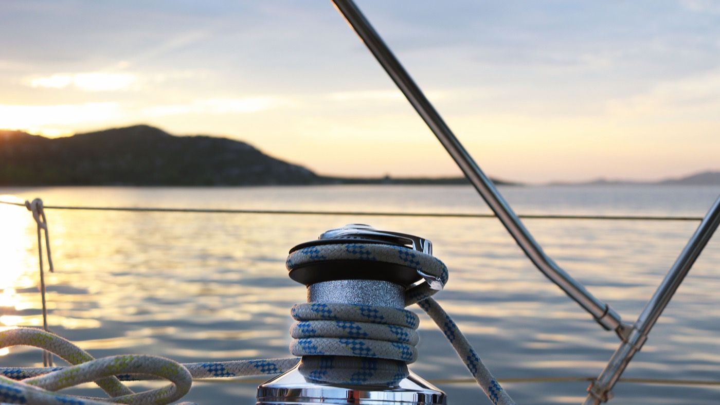 Sheet wrapped on a cockpit winch of a sailing yacht at dusk, with the sun going down behind a headland