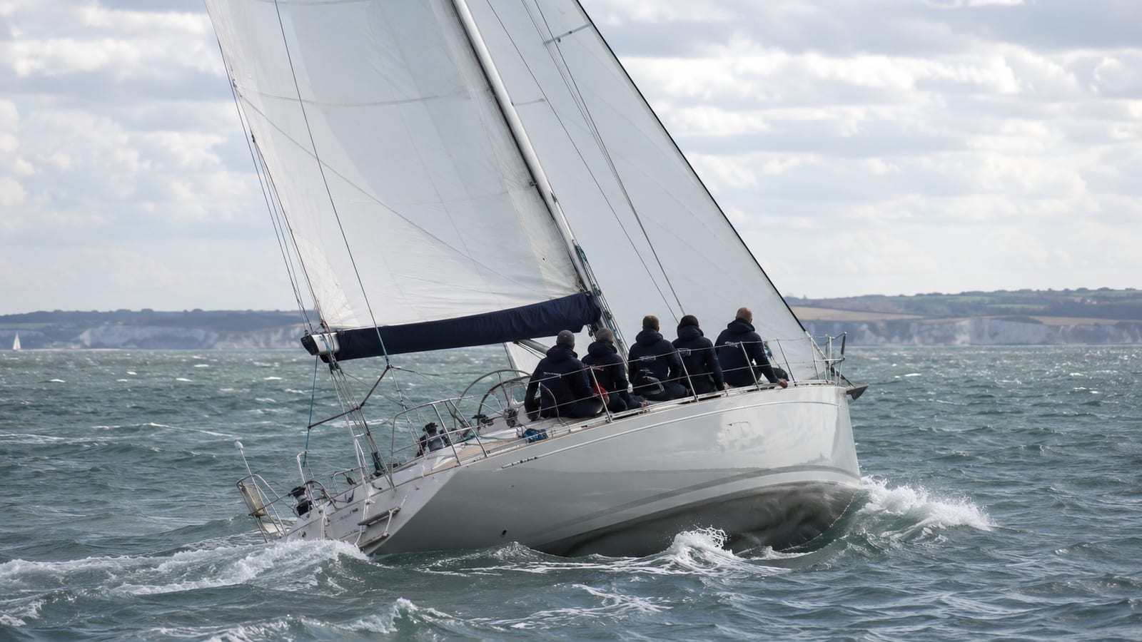 Crew sailing a yacht under full sail on the Solent with the Isle of Wight beyond