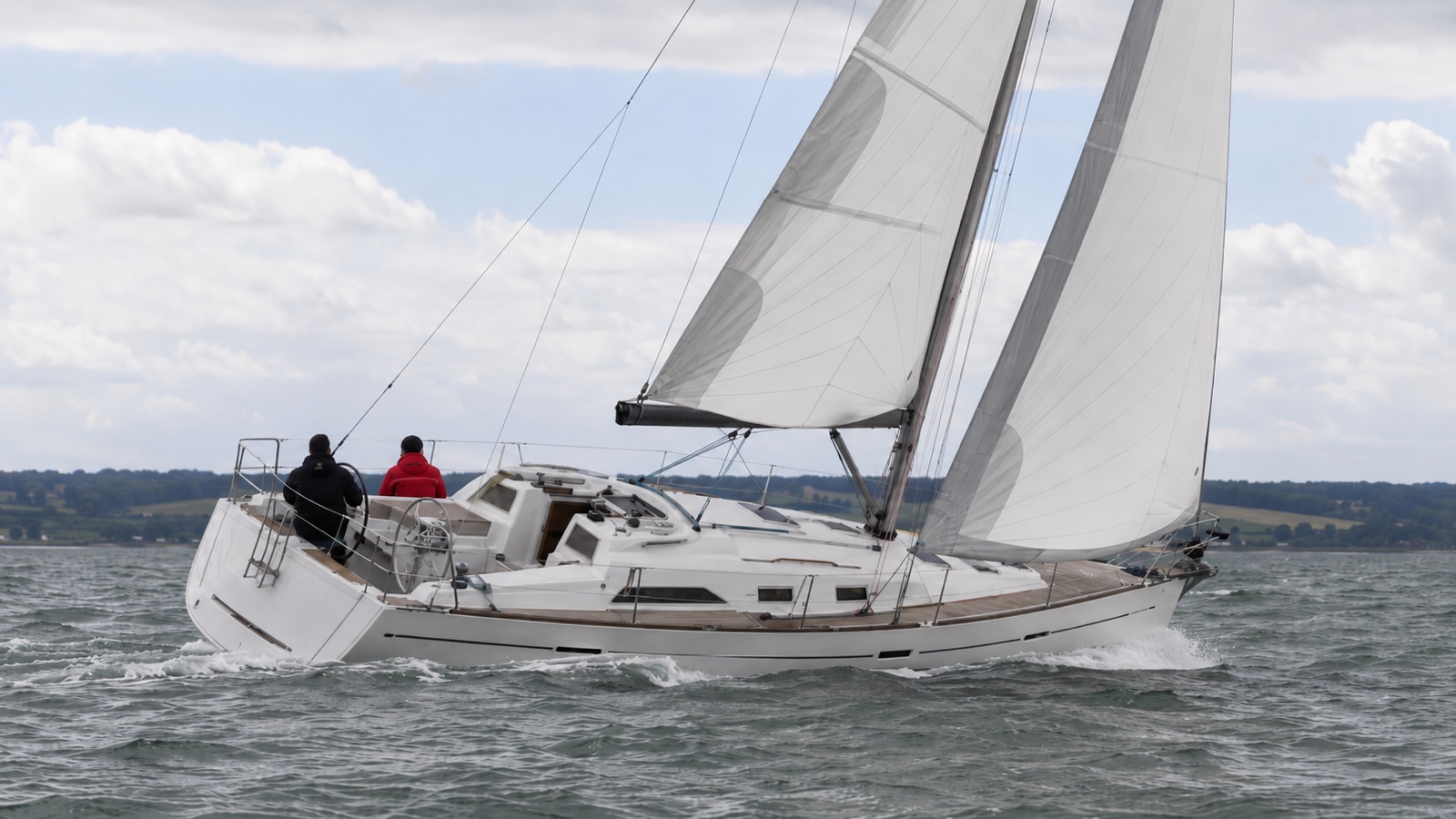 Cruising yacht sailing on a reach under full main and genoa with two crew in the cockpit